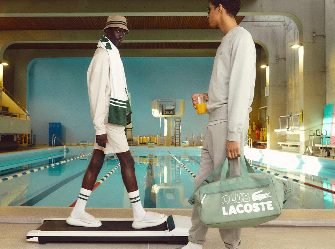 Two men in white and grey pose by the poolside, wearing the Lacoste Summer Pack Collection.